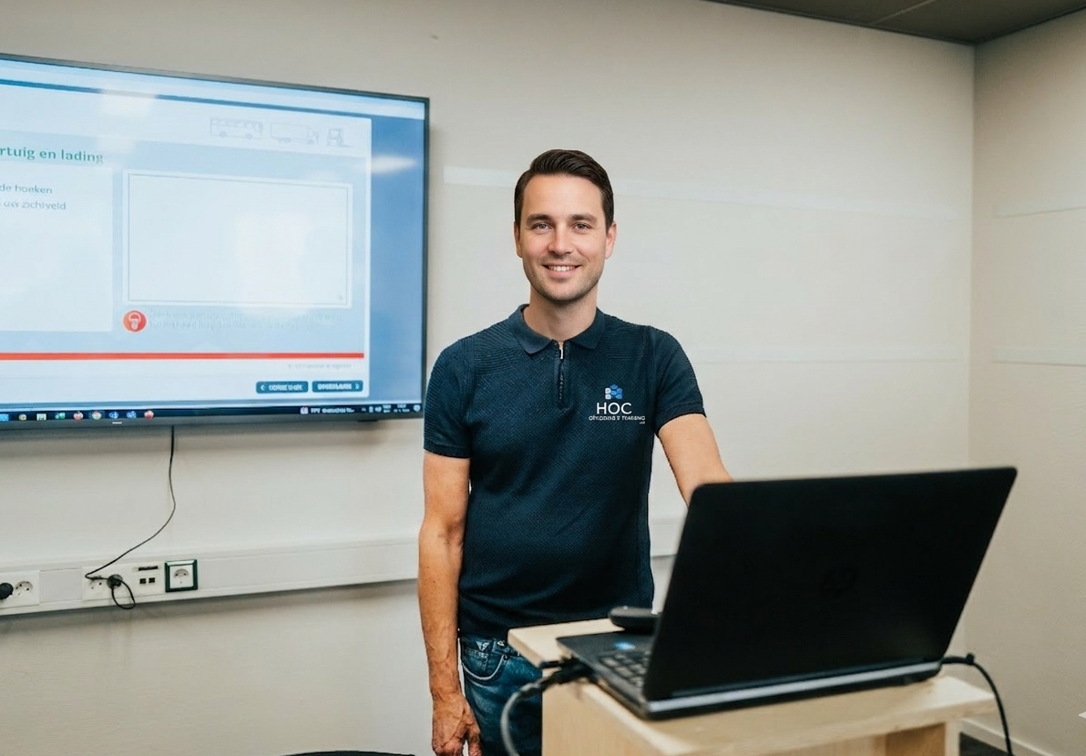 Een instructeur van HOC Opleiding & Training glimlacht in een modern klaslokaal met een laptop op een katheder en een presentatiescherm op de achtergrond.