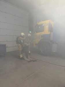 Brandweeroefening met brandweer en voertuig in rook.