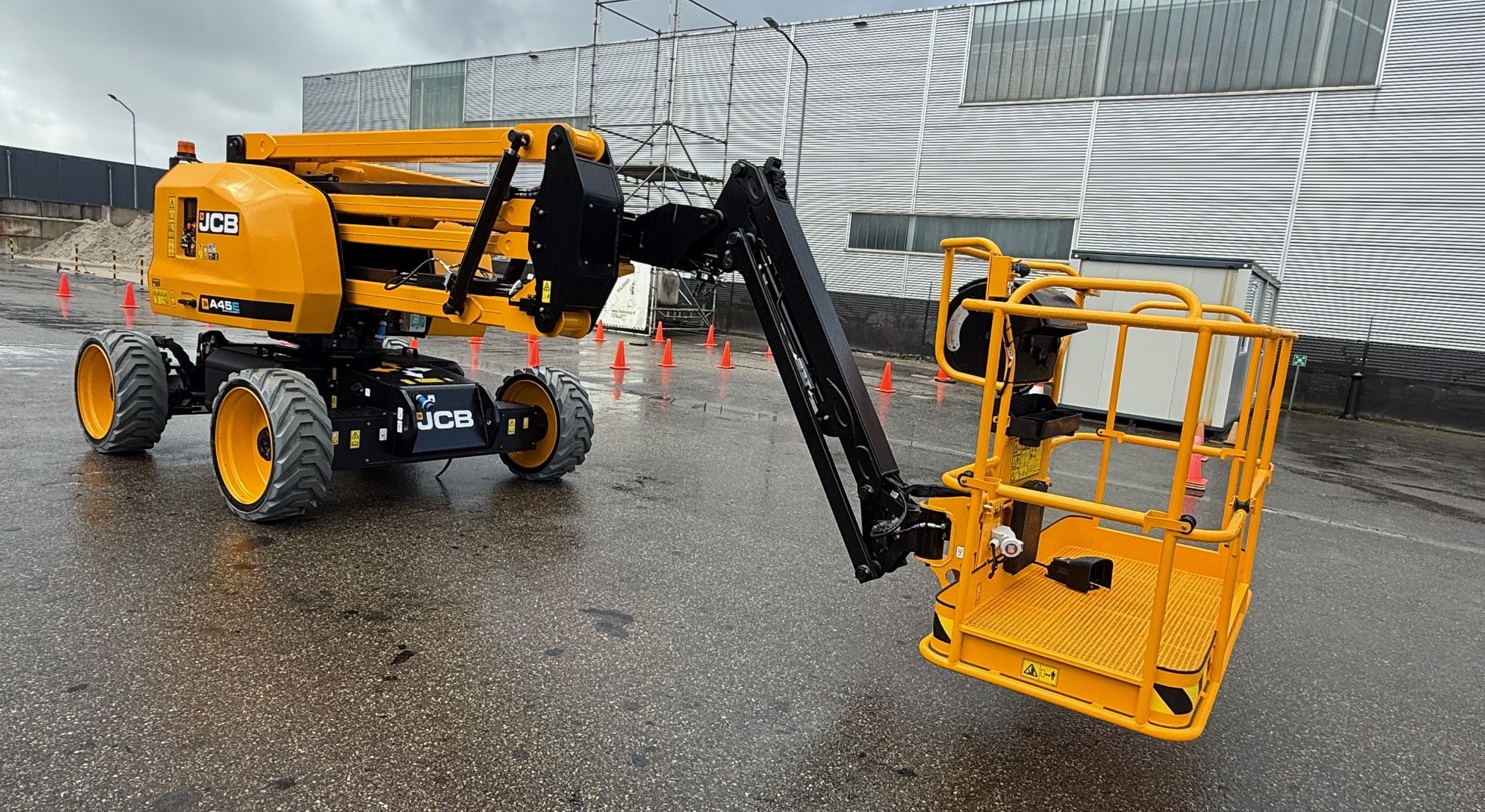 Een gele JCB A45E knikarmhoogwerker op een natte buitenlocatie, gebruikt voor een praktijkgerichte SOG hoogwerkeropleiding in Tynaarlo.
